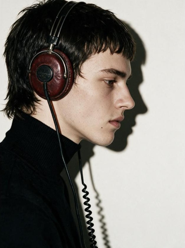 Directed: a young man in profile wearing old leather headphones, one hard light throwing his shadow on the wall.